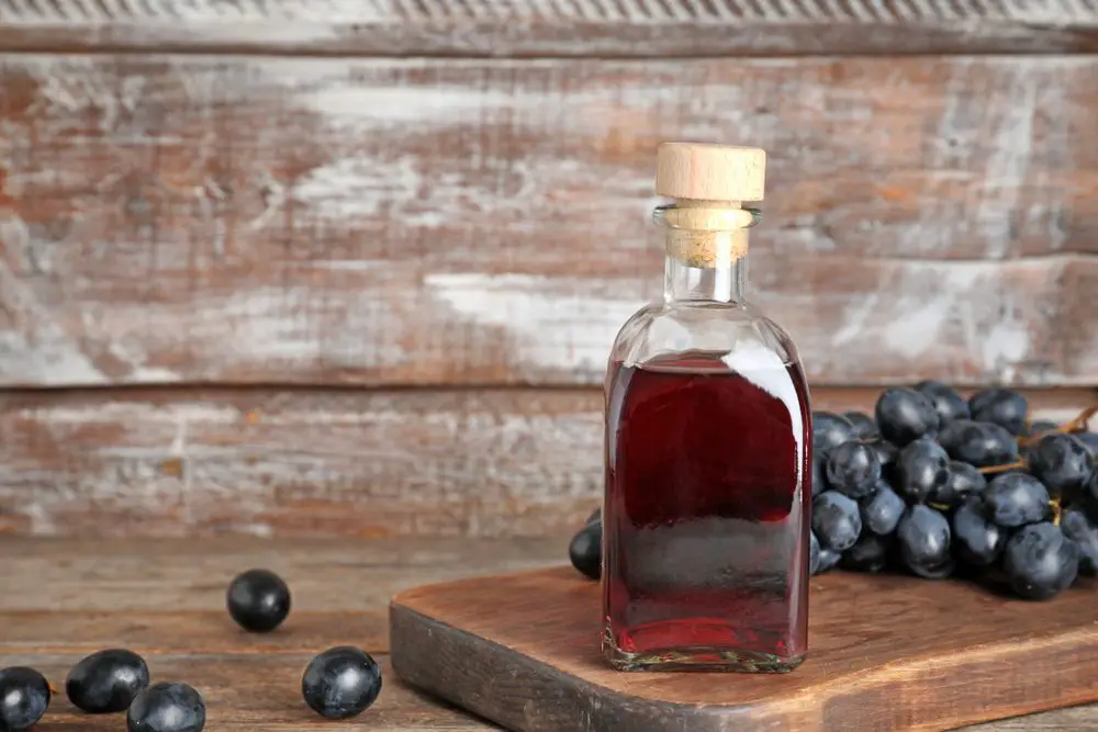 Botella de vidrio con vinagre de vino y uvas frescas sobre mesa de madera